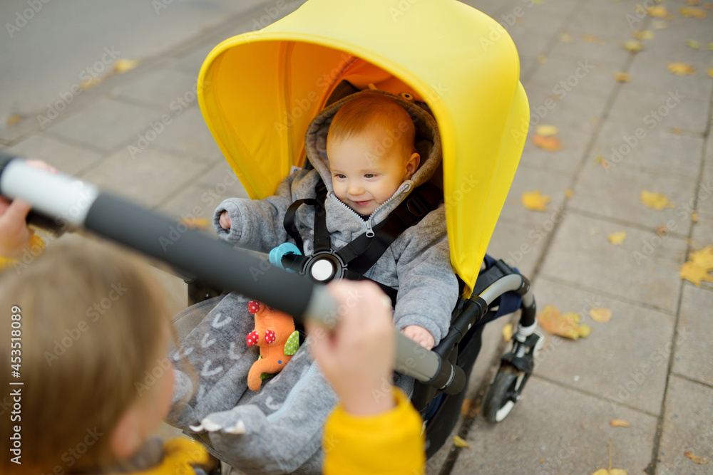 Sweet baby boy wearing warm clothes sitting in a stroller outdoors. Little child in pram. Infant kid in pushchair. Autumn walks with kids.