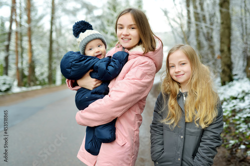 Two big sisters and their baby brother having fun outdoors. Two young girls holding their baby boy sibling on winter day. Big age difference between siblings.