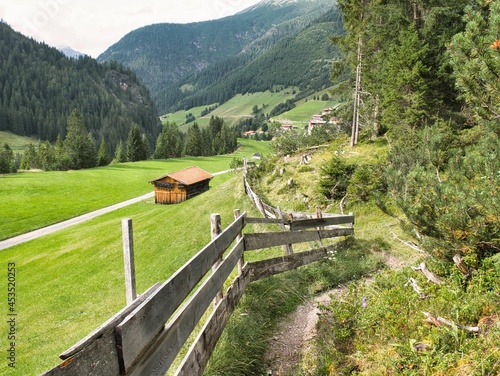 Panoramablick von einem Wanderweg oberhalb der normalen Route über einen Zaun Richtung Gramais in den Alpen in Österreich mit Wanderweg unten, hohen Bergen, Hütte und Wald photo