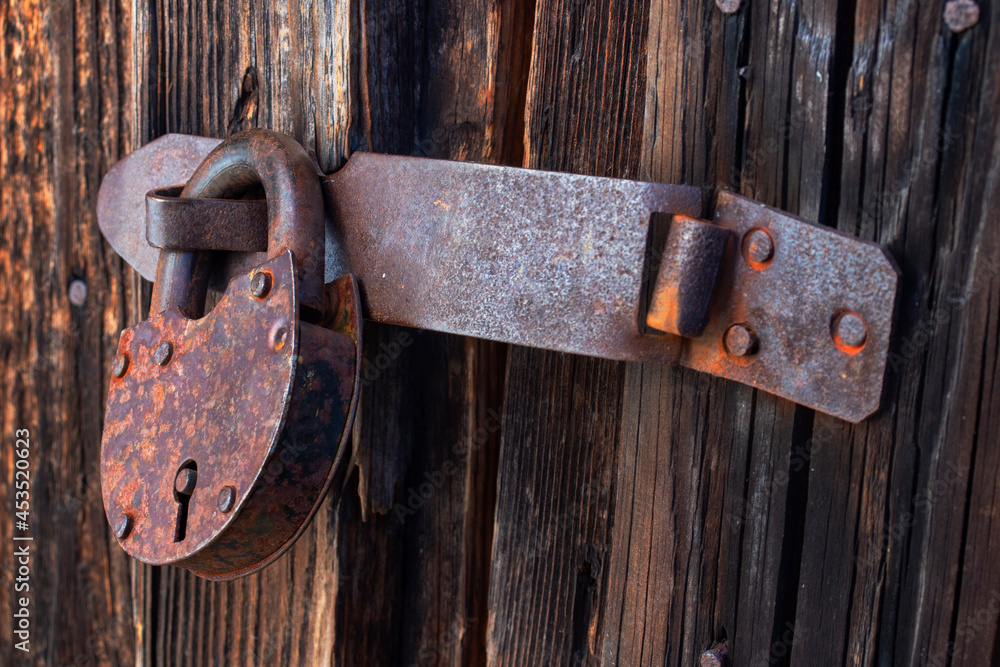 An old closed rusty barn lock hanging on the shackle of a wooden door. View from the right. Close-up. Soft light. An old closed rusty barn lock hanging on the shackle of a wooden door. View from the right. Close-up. Soft light.