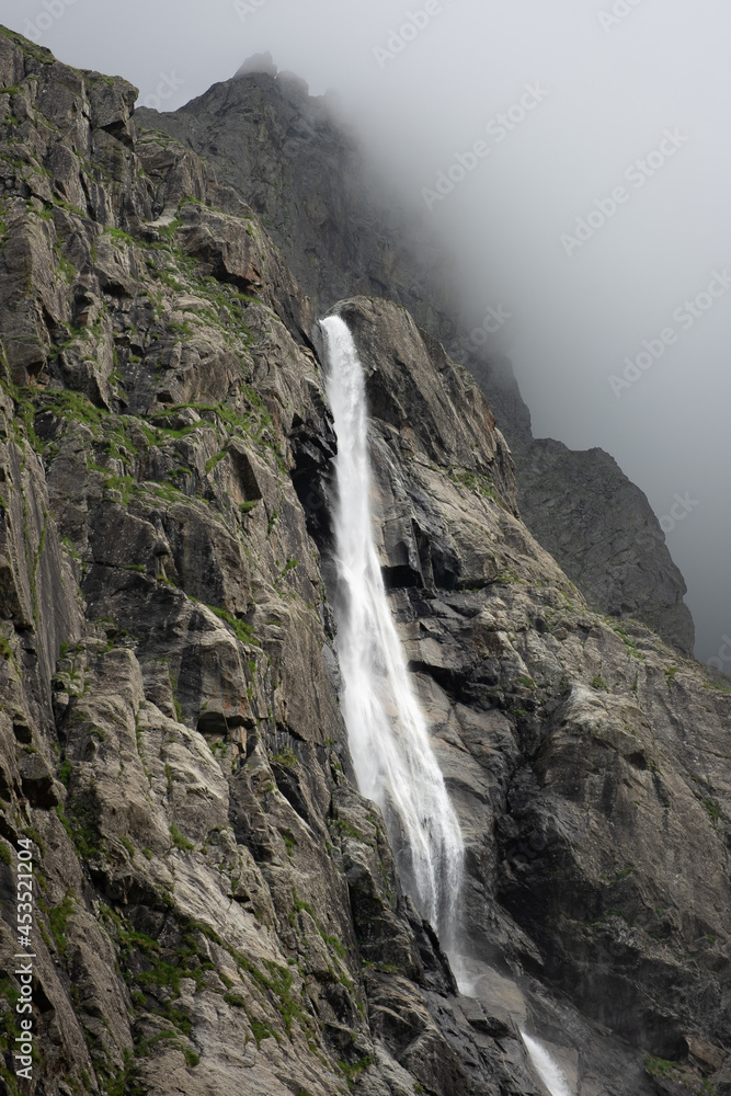Majestic Midagrabin waterfall in sunlight in cloudy summer weather. Caucasus mountains. Russia. North Ossetia Alania