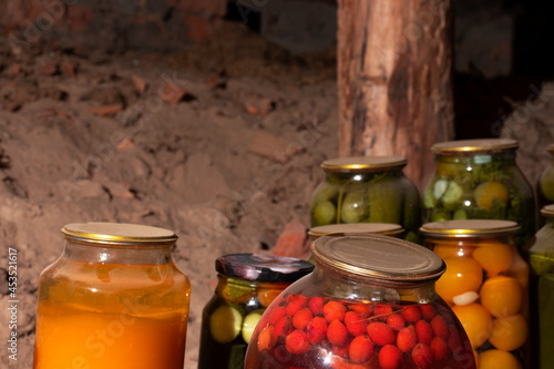 Glass jars with canned vegetables, fruits and berries are in the village cellar. Close-up. Old banks.. The foreground is a yellow and red jar.