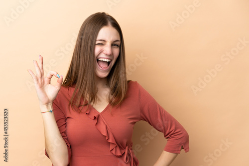 Young caucasian woman isolated on beige background showing ok sign with fingers