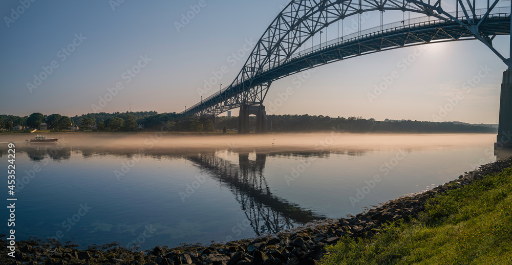 Fog Seascape under Bourne Bridge at dawn. Boat passing through Cape Cod Canal along the belt of fog. Tranquil Cape Cod image for water sports, vacation guides, and open space concepts.