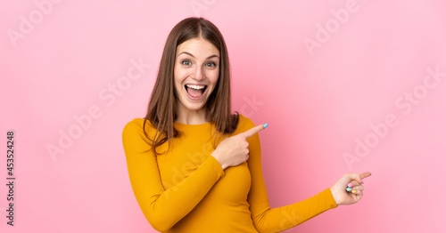 Young caucasian woman isolated on pink background surprised and pointing side