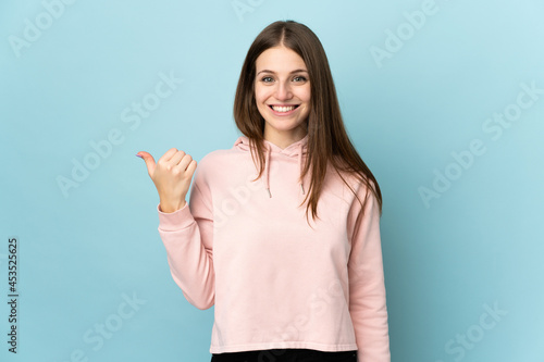 Young caucasian woman isolated on blue background pointing to the side to present a product