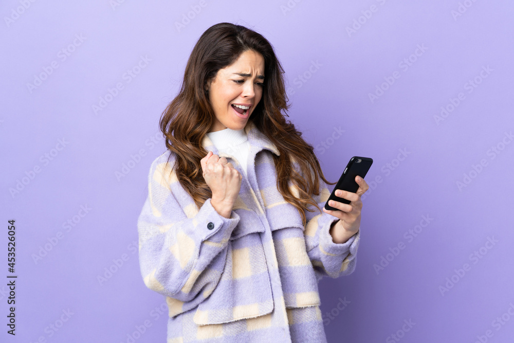 Woman over isolated purple background with phone in victory position Woman over isolated purple background with phone in victory position