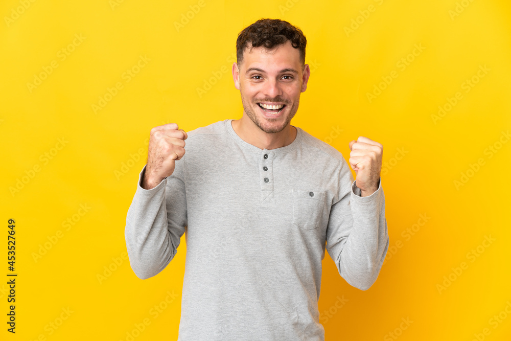 Young caucasian handsome man isolated on yellow background celebrating a victory in winner position Young caucasian handsome man isolated on yellow background celebrating a victory in winner position