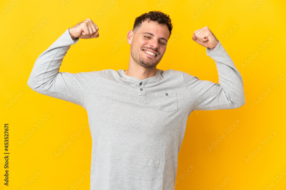 Young caucasian handsome man isolated on yellow background doing strong gesture Young caucasian handsome man isolated on yellow background doing strong gesture