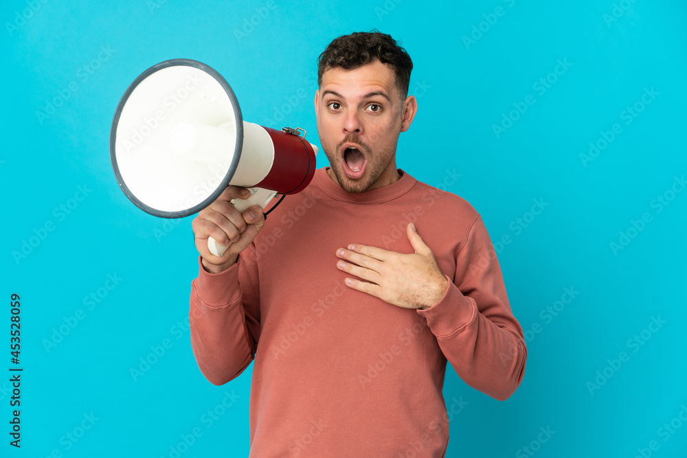 Young caucasian handsome man isolated on blue background shouting through a megaphone with surprised expression Young caucasian handsome man isolated on blue background shouting through a megaphone with surprised expression