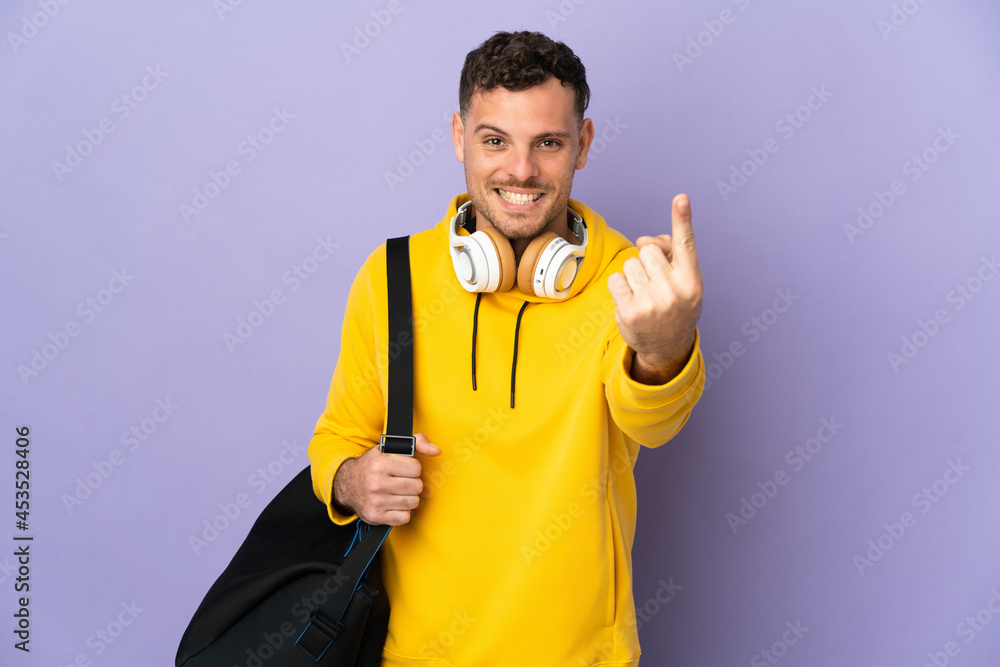 Young sport caucasian man with bag isolated purple background doing coming gesture Young sport caucasian man with bag isolated purple background doing coming gesture