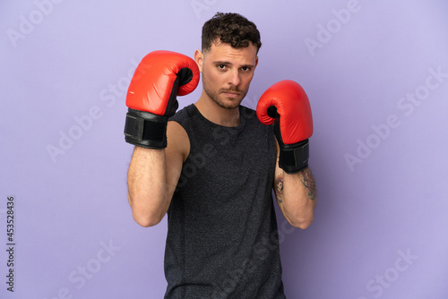 Young caucasian handsome man isolated on purple background with boxing gloves © luismolinero