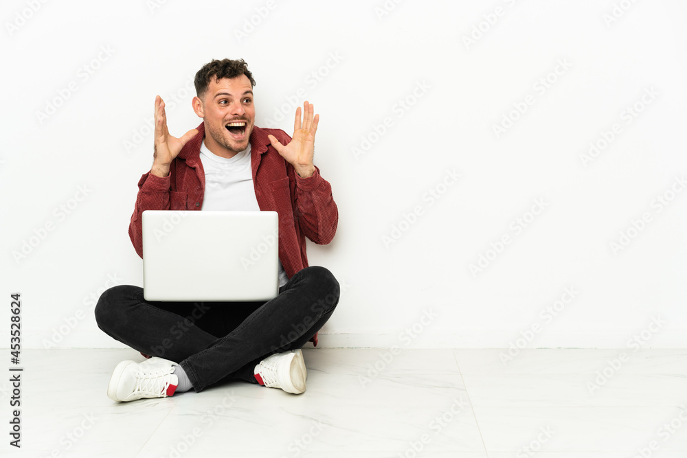 Young handsome caucasian man sit-in on the floor with laptop with surprise facial expression Young handsome caucasian man sit-in on the floor with laptop with surprise facial expression