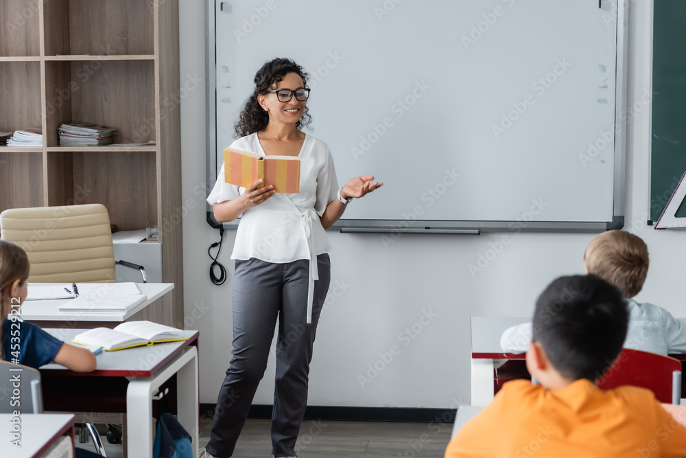 african american teacher holding book and pointing with hand during lesson african american teacher holding book and pointing with hand during lesson