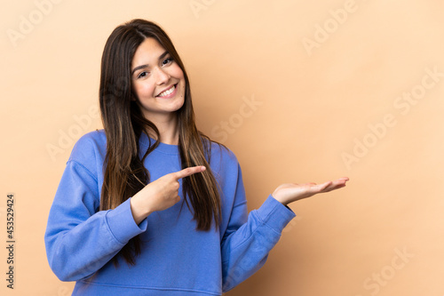 Teenager Brazilian girl over isolated background holding copyspace imaginary on the palm to insert an ad