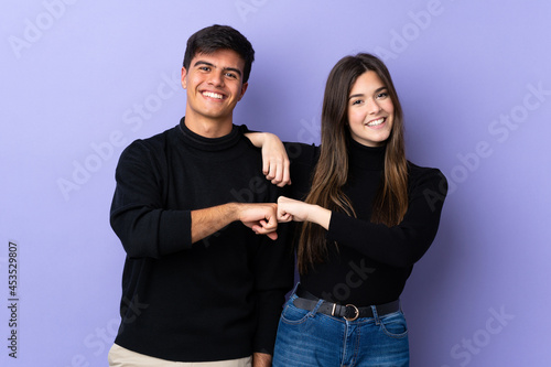 Young couple over isolated purple background bumping fists