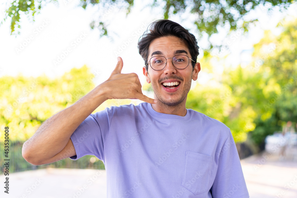 Young caucasian man at outdoors in a park making phone gesture. Call me back sign Young caucasian man at outdoors in a park making phone gesture. Call me back sign