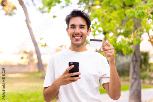 Young caucasian man in a park buying with the mobile with a credit card