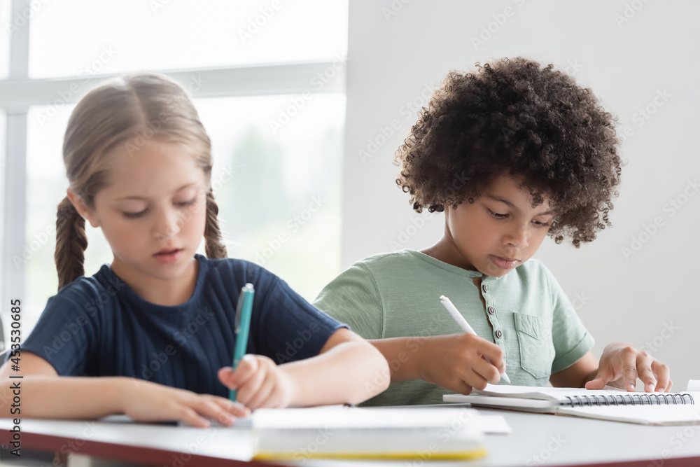 interracial kids writing in notebooks during lesson interracial kids writing in notebooks during lesson