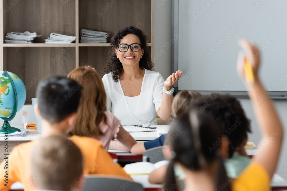 Ταπετσαρία positive african american teacher pointing at blurred girl raising hand in class