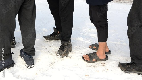 Barefoot migrant standing on the snow. Migrants wait in line for food in camp 