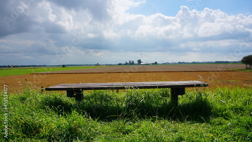 Alone bench in nature. Abandoned and no people. Agricultural farmland in the background and summer weather with cloudy sky.