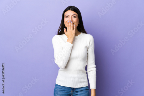 Young brunette woman over isolated purple background covering mouth with hand