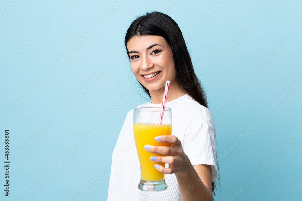 Young brunette girl over isolated blue background holding an orange and an orange juice Young brunette girl over isolated blue background holding an orange and an orange juice