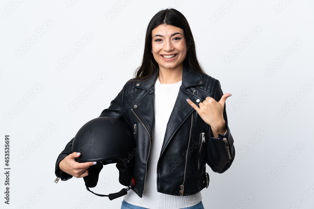 Young woman holding a motorcycle helmet over isolated white background making phone gesture Young woman holding a motorcycle helmet over isolated white background making phone gesture