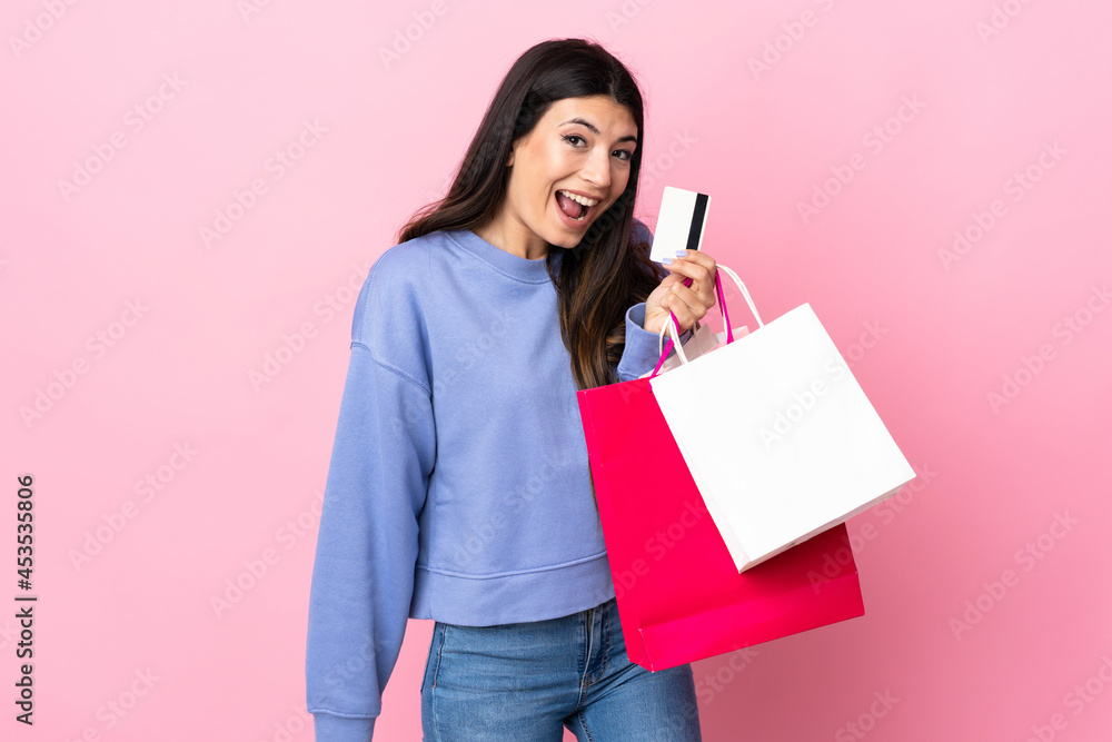 Young brunette girl over isolated pink background holding shopping bags and a credit card Young brunette girl over isolated pink background holding shopping bags and a credit card