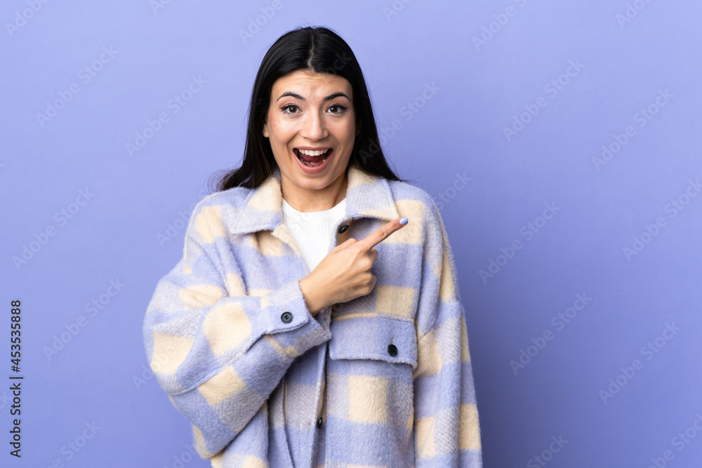 Young brunette woman over isolated purple background surprised and pointing side Young brunette woman over isolated purple background surprised and pointing side