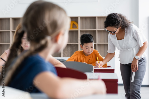 african american teacher helping asian boy during lesson in classroom