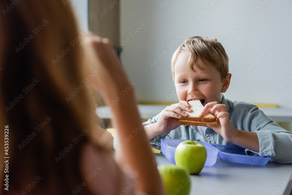 schoolboy eating sandwich near girl on blurred foreground