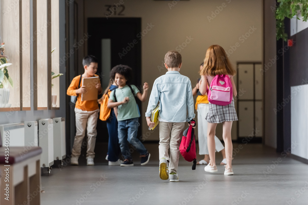 multiethnic schoolkids with backpacks and notebooks in school corridor