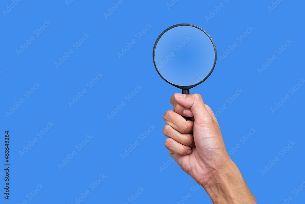 Hand holding a magnifying glass on a blue background Hand holding a magnifying glass on a blue background