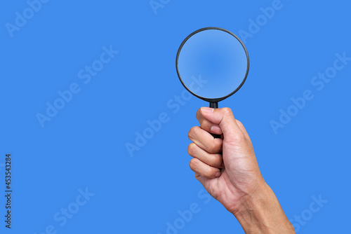 Hand holding a magnifying glass on a blue background