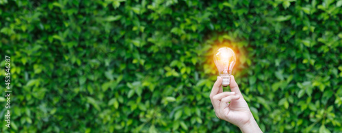 Hand holding Light bulb with light flare green nature background. eco innovation environmental and creative concepts. copy space banner.