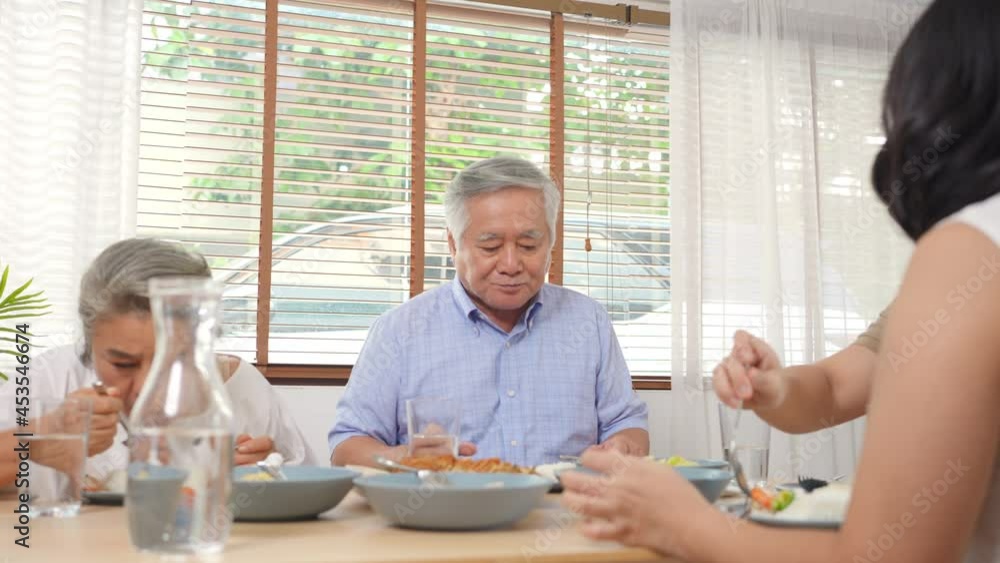 Asian family having dinner together at home. Smiling adult couple with senior parents enjoy eating and sharing thai food on dining table. Happy family spending time together on weekend vacation. Asian family having dinner together at home. Smiling adult couple with senior parents enjoy eating and sharing thai food on dining table. Happy family spending time together on weekend vacation.