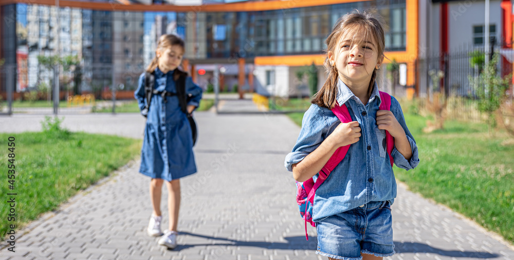 Little girls, primary school students with backpacks go from school. Little girls, primary school students with backpacks go from school.