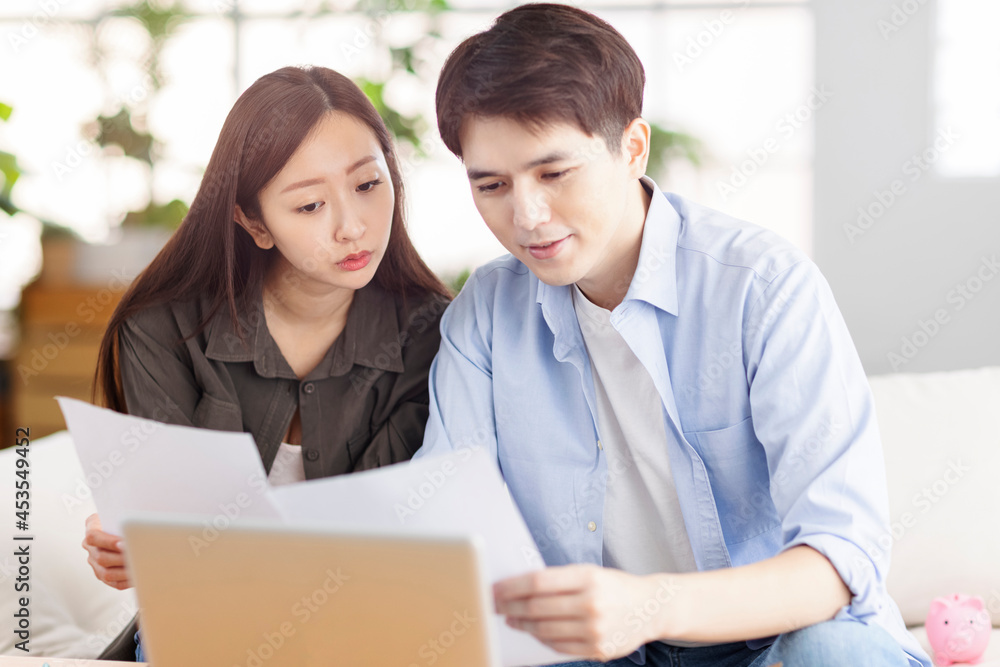 Young husband and wife holding paperwork and using laptop at home. Young husband and wife holding paperwork and using laptop at home.