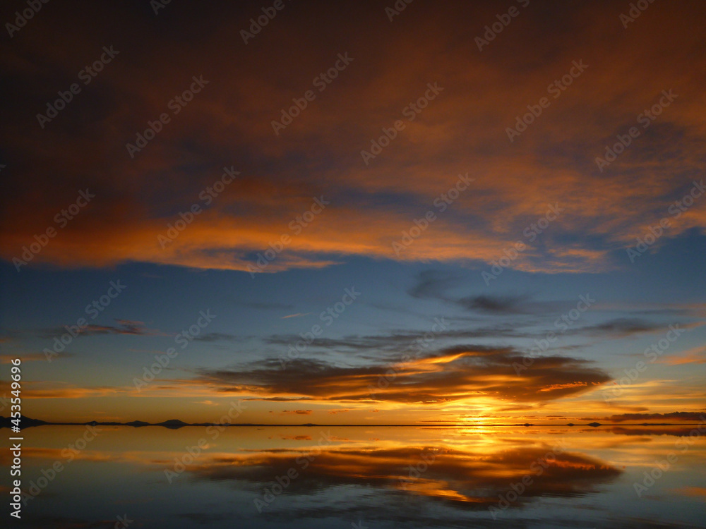 ボリビアのウユニ塩湖にて水面に鏡のように反射するオレンジ色の夕日