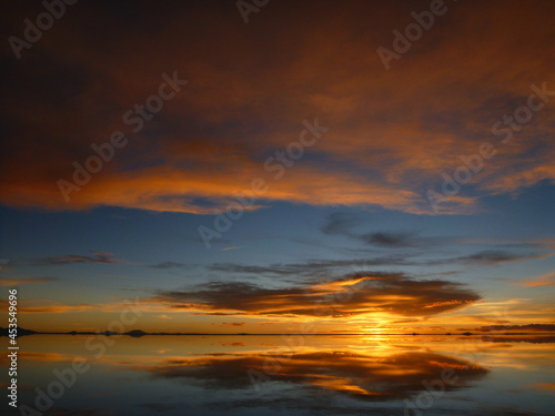 ボリビアのウユニ塩湖にて水面に鏡のように反射するオレンジ色の夕日
