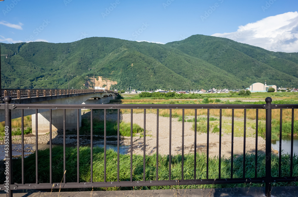 Fototapeta premium summer scenery of countryside, chikuma river and mountain seen in front of safety fence on side walk in nagano prefecture, japan