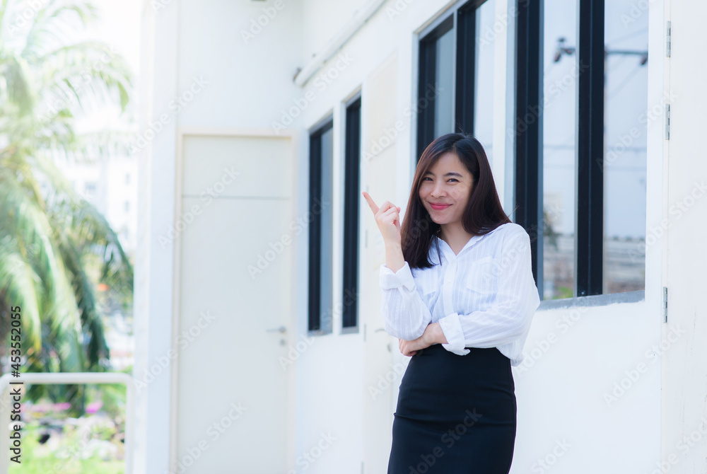 attractive adult business woman asian girl finger point up with happy and smile front of her office. attractive adult business woman asian girl finger point up with happy and smile front of her office.
