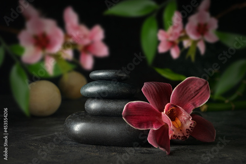 Stack of spa stones and beautiful flowers on dark background