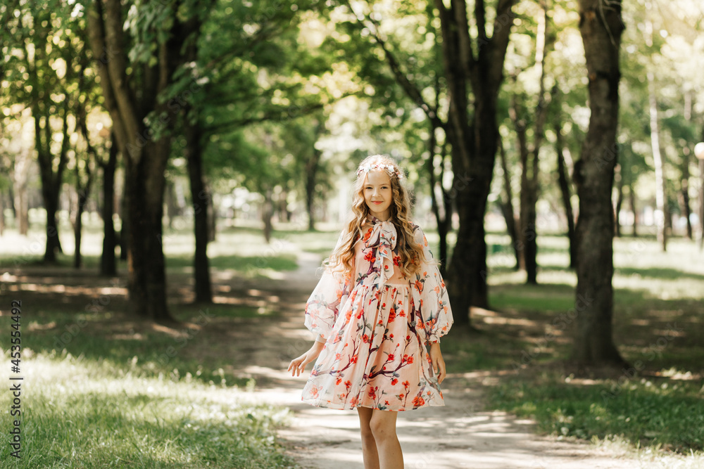 A girl with long blonde hair in a beautiful dress walks in the park in the summer on a sunny day A girl with long blonde hair in a beautiful dress walks in the park in the summer on a sunny day