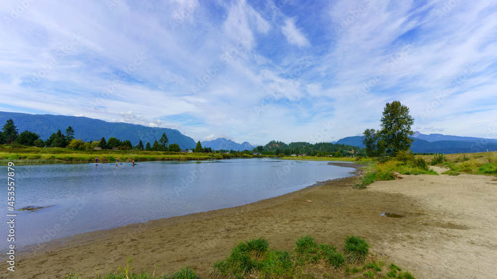 Paddleboarders on peaceful Alouette River near Pitt Meadows, BC, on a summer day with mountain backdrop.