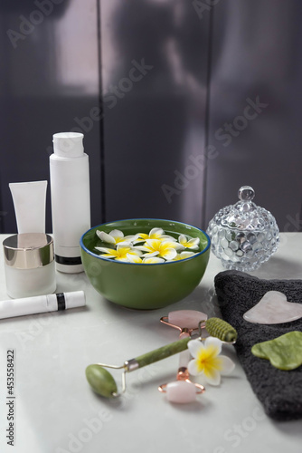 Beautiful spa composition with plumeria flowers. Face roller and guasha massager. Facial skin care  anti age products and creme. Chinese Gua Sha massage tools.