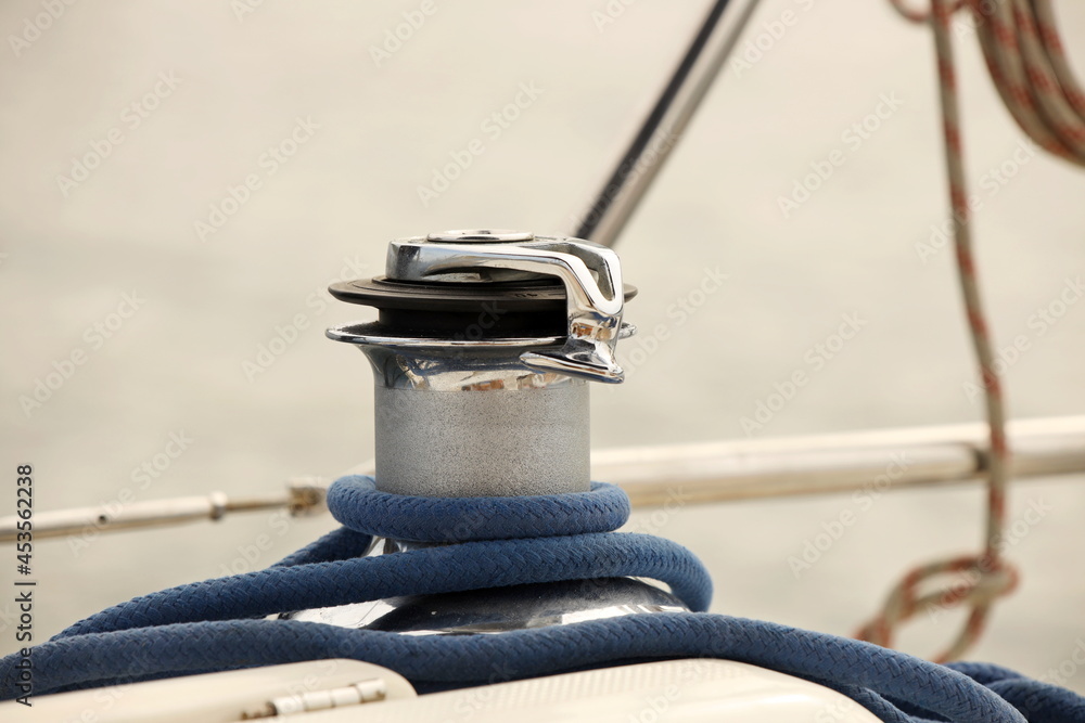 Obraz premium A winch on a sailing yacht for pulling up files and sheets against the background of the summer sea. Outfit of a sailing yacht. Facilitating human labor on board. Mar practice in a yachting school.