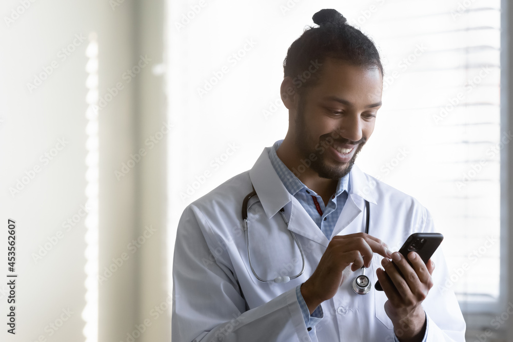 Smiling millennial generation african american biracial gp doctor physician  using cellphone, reading message email with pleasant news, communicating  online with patient or web surfing in clinic. Stock Photo | Adobe Stock